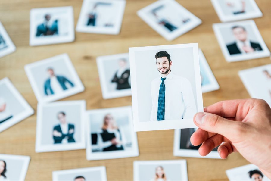 An HR professional's hand holds a chosen candidate's photo, with several other applicant photos spread on the desk.