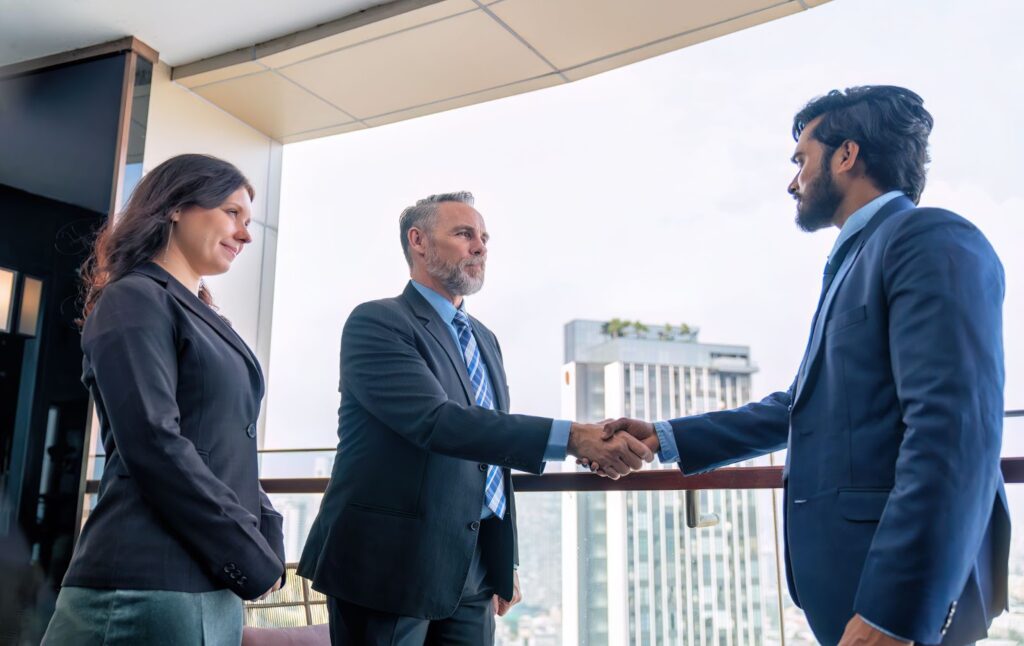 An executive from a legal firm shakes hands with a company CEO as his colleague stands beside him.