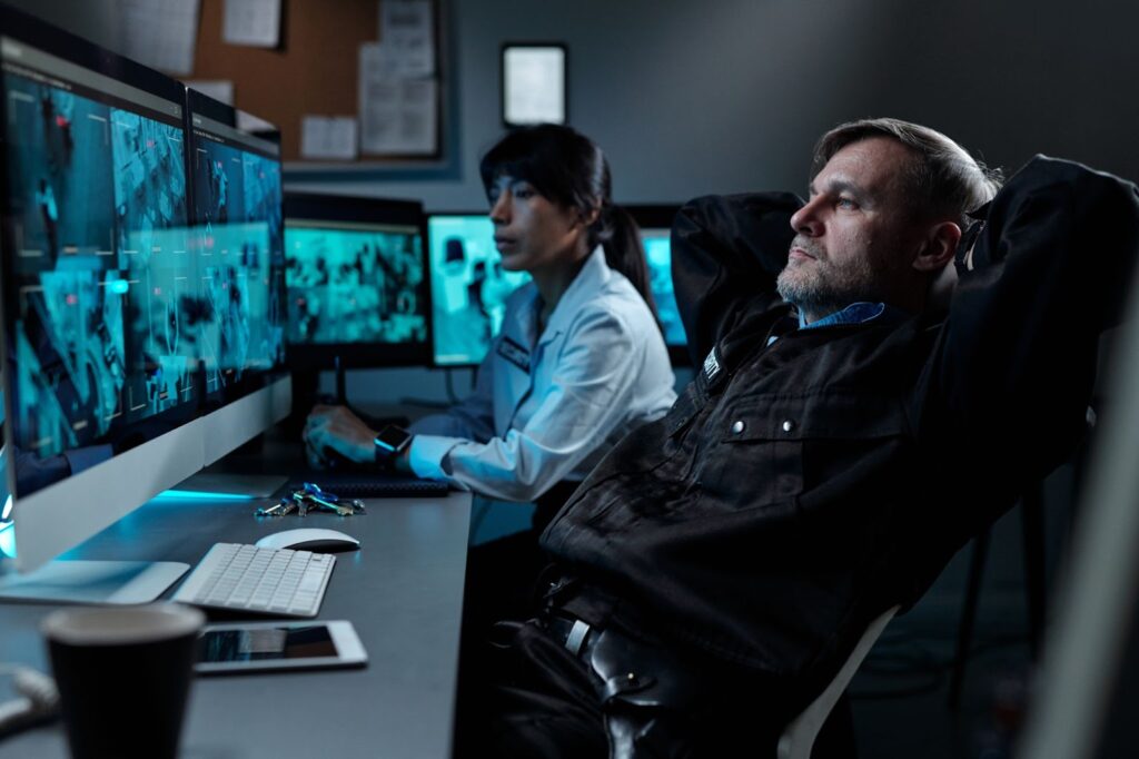 A senior investigator reviews the CCTV footage in the control room with a female security personnel.