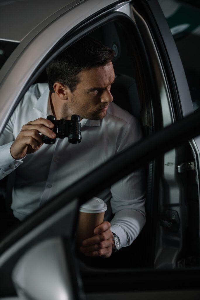 A private investigator at night surveilling with a cup of coffee and binoculars.