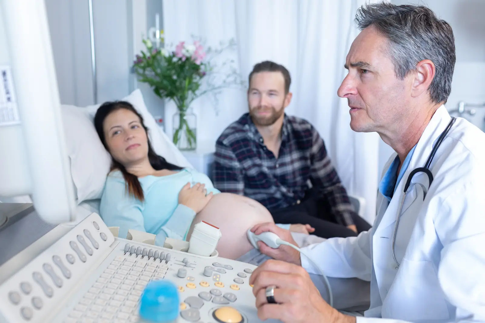 A man and a pregnant woman are watching as a doctor performs an ultrasound.