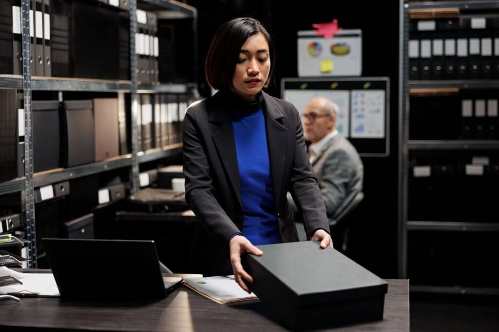 A woman in a dark office opens a black box.