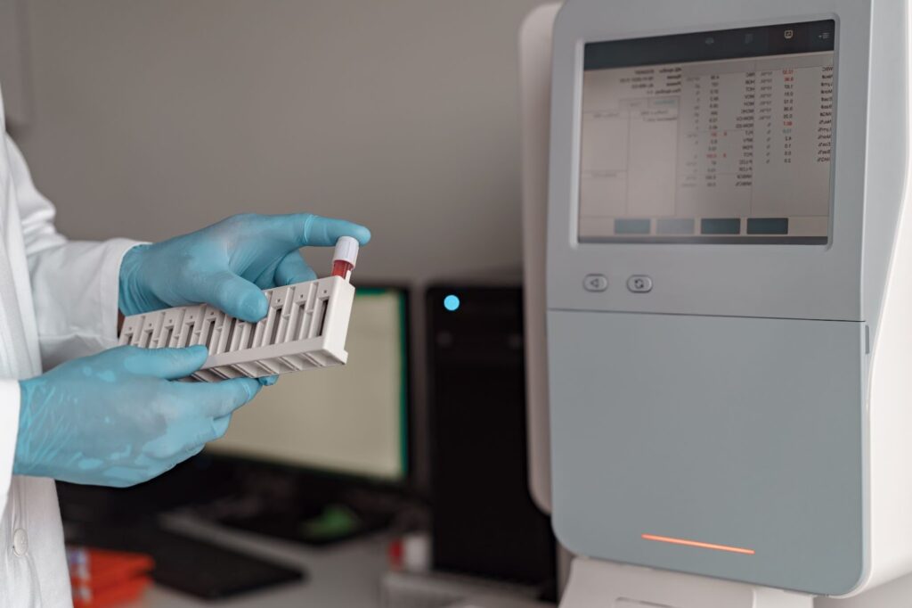 A lab worker is inserting a tube of bloodwork into a machine.