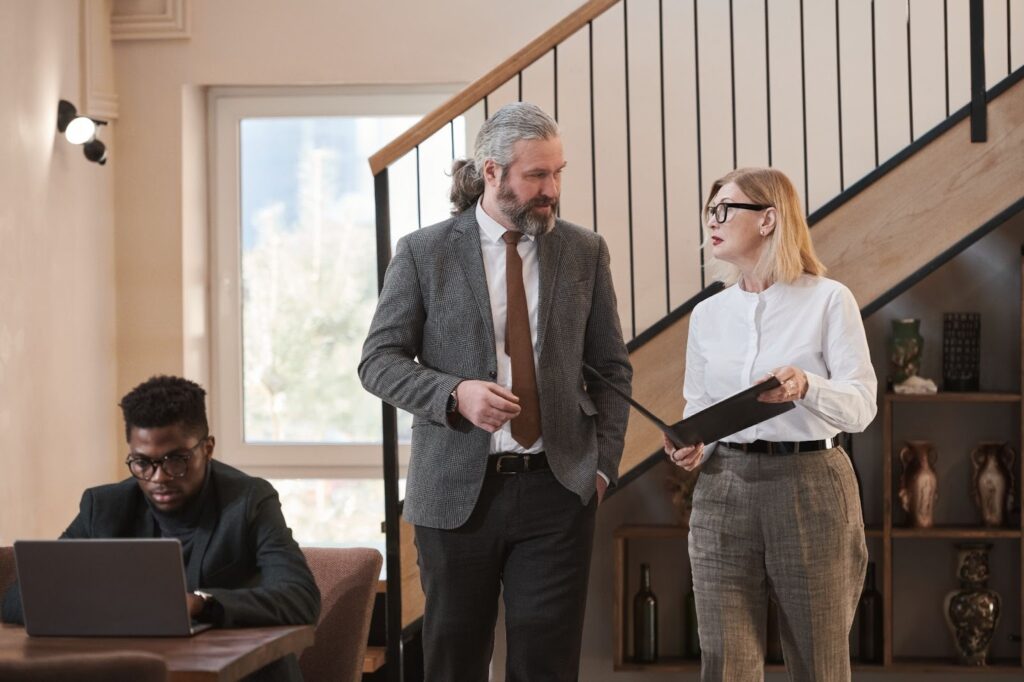 Insurance investigator interviewing a claimant’s former colleague during a workplace fraud inquiry, with another employee in the background.