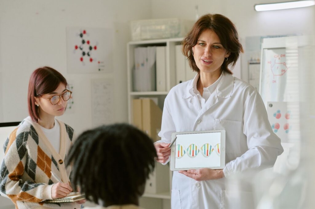 Researcher explaining DNA test results to two colleagues inside a genetics lab.
